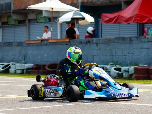 Davi Jimenez pilotando o kart número 58 em uma curva de pista de terra batida cercada por pneus