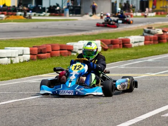 Davi Jimenez pilotando o kart número 12 em pista com arquibancada e guarda-sóis ao fundo