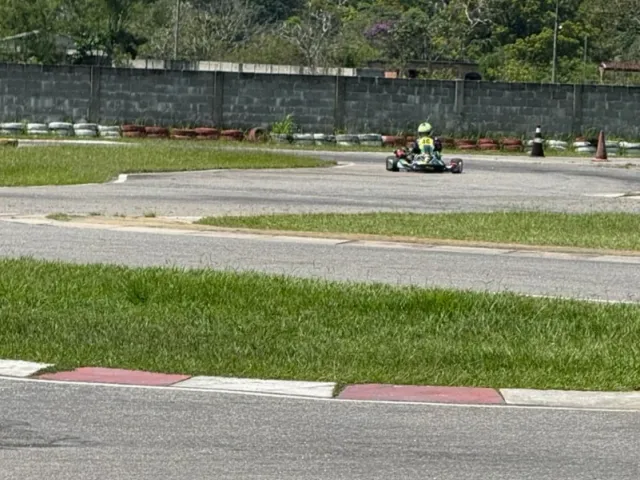 Kart número 12 em curva de pista de terra, visto à distância entre a grama